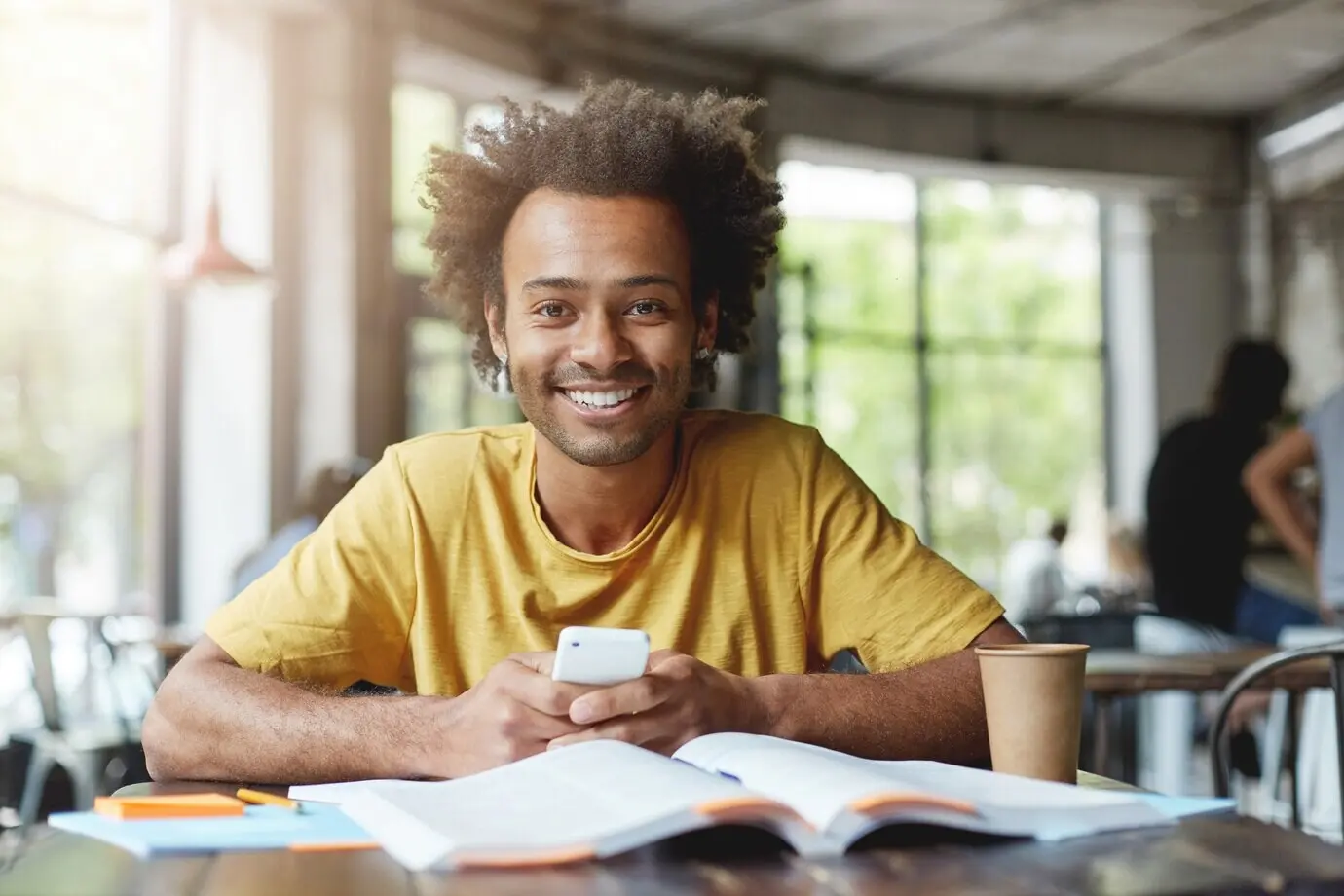Fröhlicher männlicher Student, der ein gelbes T-Shirt trägt und in einem Café sitzt.